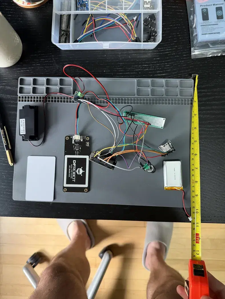 ESP32, NFC reader, audio amplifier, battery, speaker, and wiring laid out on a workbench